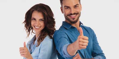 Smiling couple standing back to back giving thumbs up sign