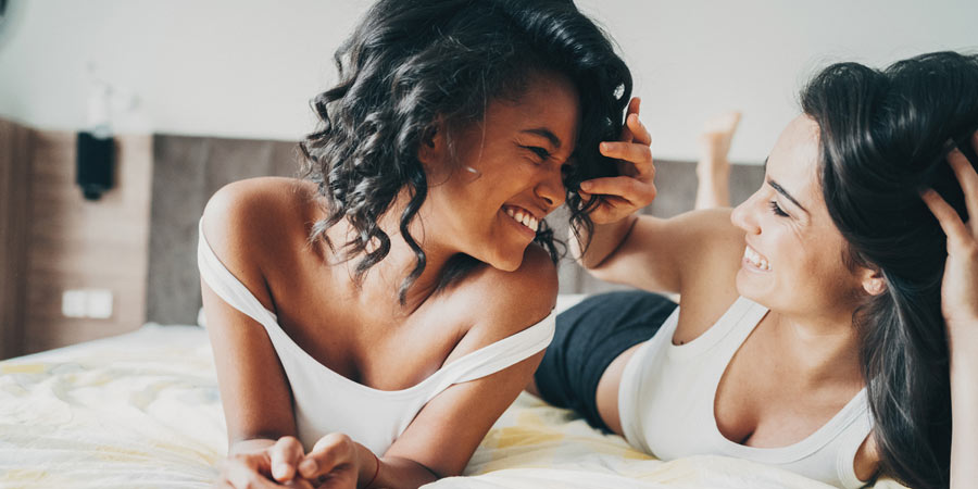 Two bisexual women in bed sharing an intimate moment and laughing