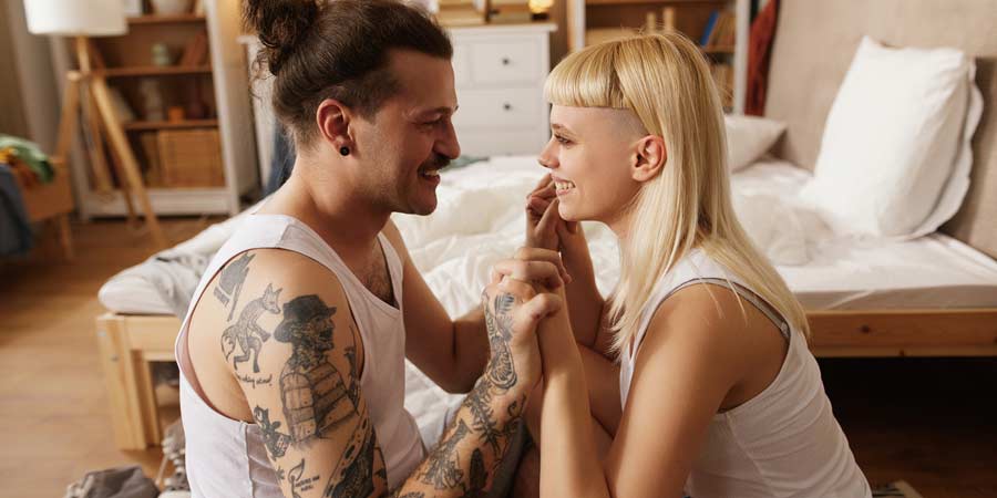 Sexy young couple sitting on the bedroom floor smiling at each other after a satisfying hook up