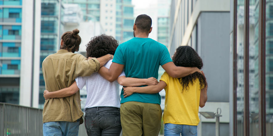 Two men and two women walking away from camera arm in arm