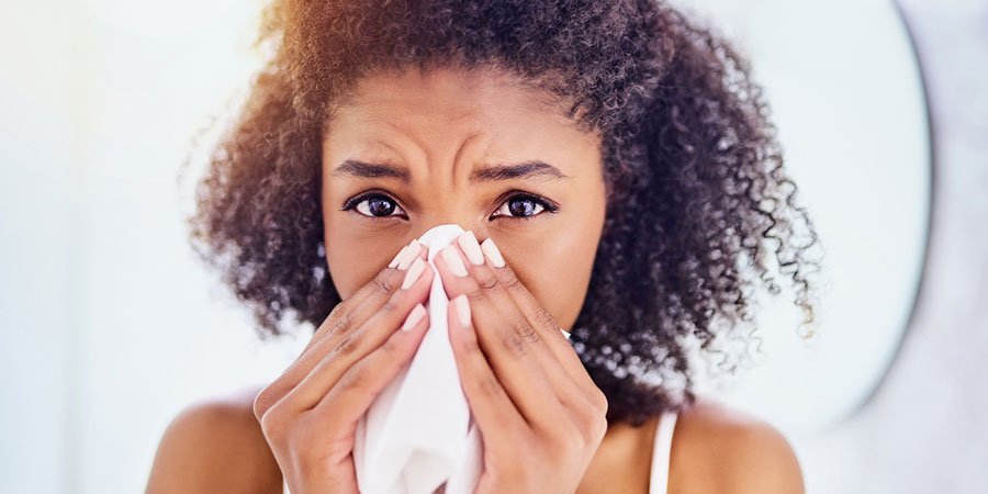 Attractive dark skinned woman using a hanky to clear her stuffy nose