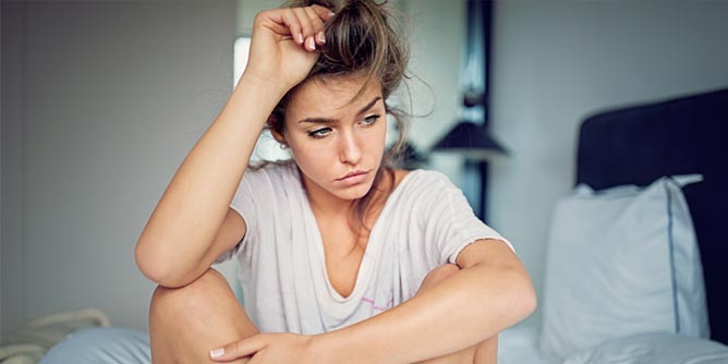 Young woman sitting cross legged in bed looking broken hearted