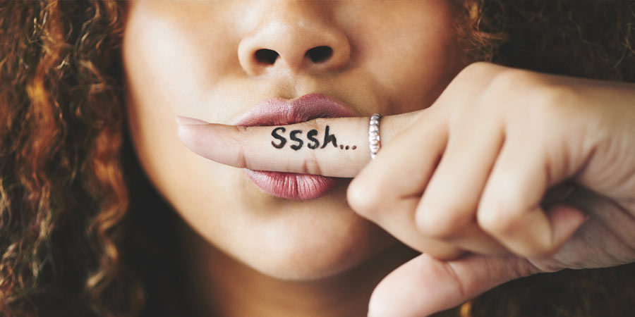 Woman with long curly hair making a shhhh gesture with her finger